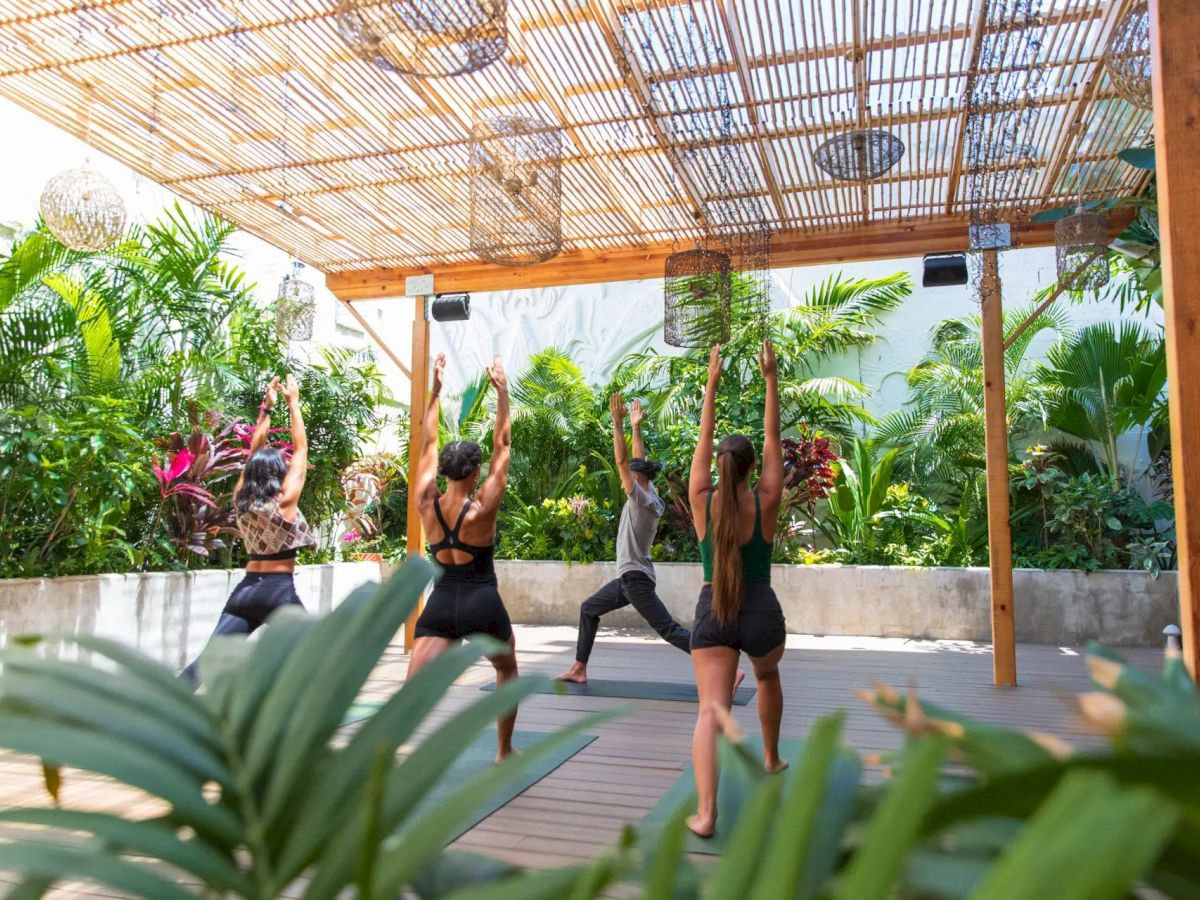 A group of people practicing yoga outdoors under a bamboo canopy, surrounded by lush greenery, creates a serene atmosphere.