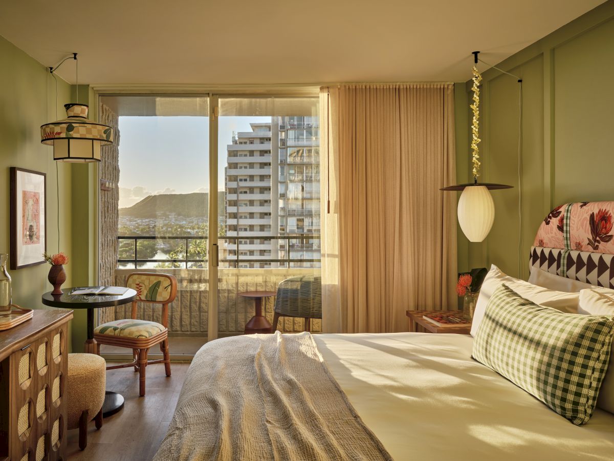 Une chambre d'h&ocirc;tel confortable avec un lit king-size baign&eacute; de soleil, des murs verts, des lampes lanternes vintage, un coin bureau, un balcon avec vue sur les immeubles de la ville et des coussins &agrave; motifs.