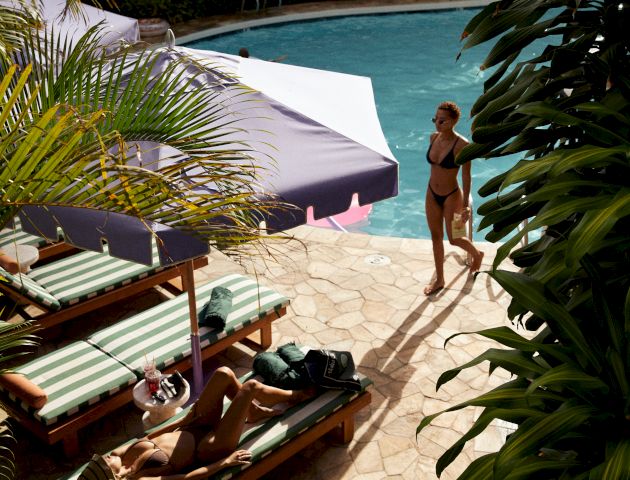This image shows a sunny tropical beach with turquoise water, white sand, lounge chairs, and a thatched-roof hut along the shoreline.