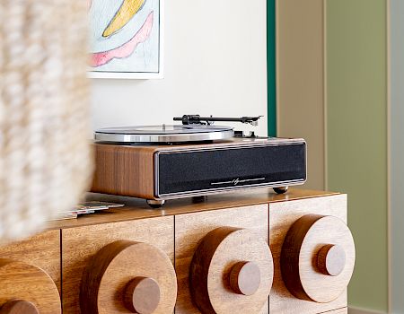 A wooden record player/turntable sits on a decorative cabinet, with colorful wall art hanging above it.