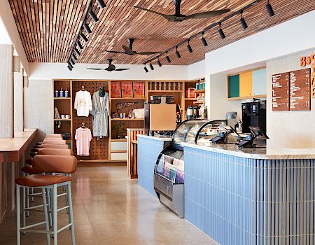 A modern café interior with a glass display counter, espresso machines, menu boards, and sleek ceiling fans overhead.