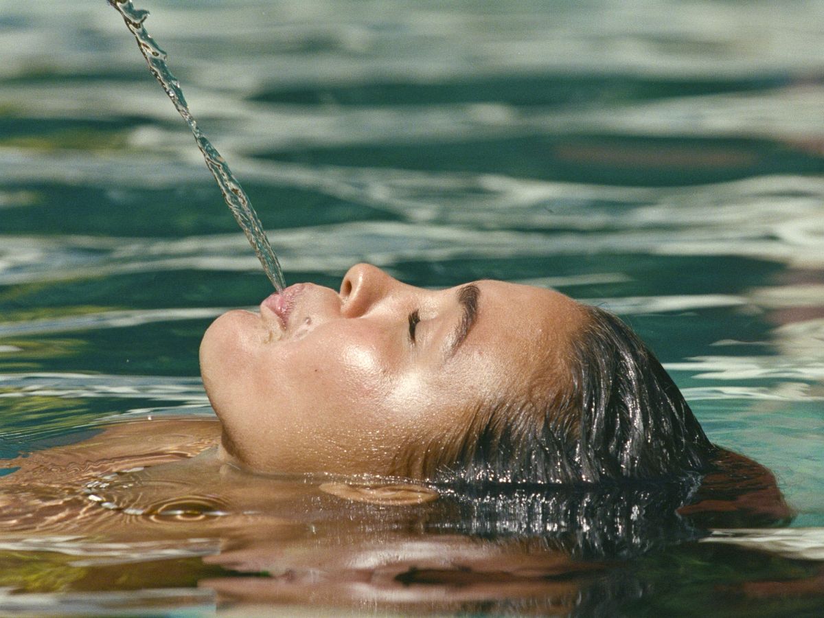 Une personne flotte dans l'eau de mer tandis qu'un filet d'eau lui ruisselle sur le visage, photo prise sur la plage.